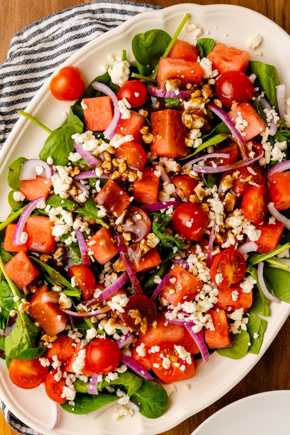 White serving platter loaded with fresh watermelon, grape tomatoes, red onion, spinach and feta cheese is an easy to make side dish for any spring or summer gathering.