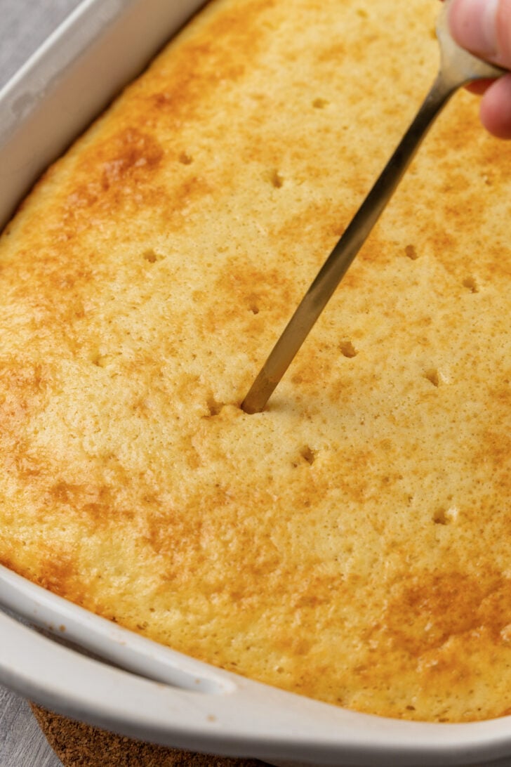 white bake made with a box mix in a white dish being poked with a fork.