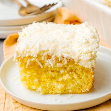 Slice of coconut cake made with a box mix, whipped topping, and coconut served on a white plate for dessert.