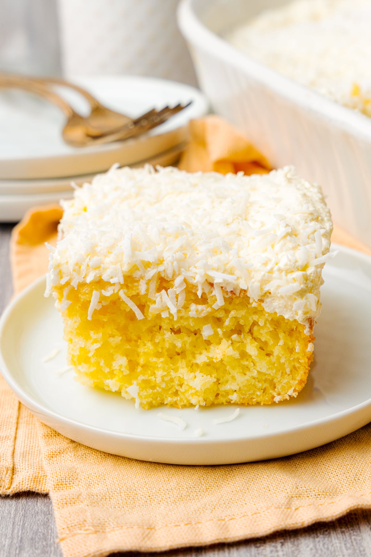 Slice of coconut cake made with a box mix, whipped topping, and coconut served on a white plate for dessert.