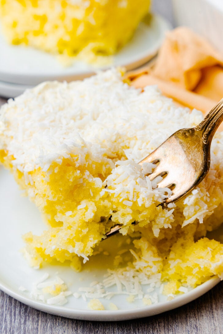Slice of coconut cake being served with a silver fork on a white plate, for dessert is made with a cake box and easy to make.
