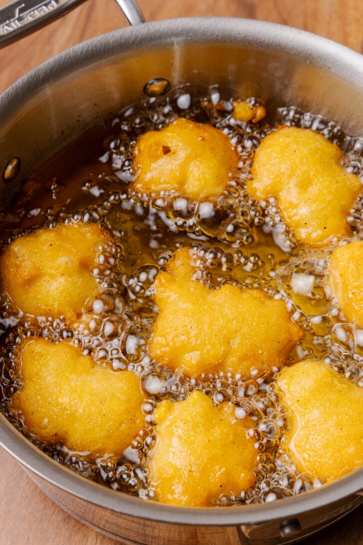 Metal pan with hot, bubbling vegetable oil cooking corn fritters.