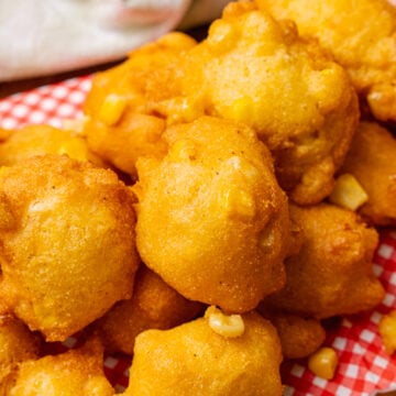 Stack of fried corn fritter stacked on a red and white paper napkin on a wooden serving board.