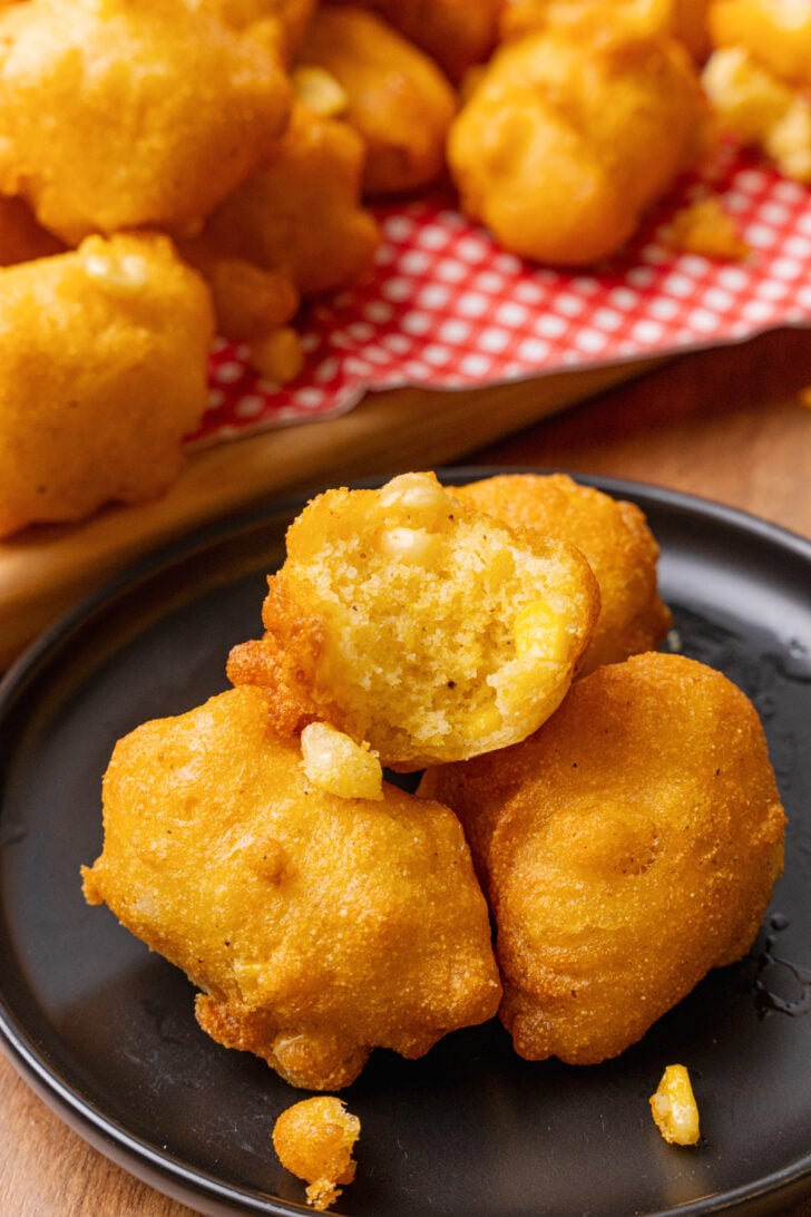 Whole fried corn frittiers made with corn kernels served on a black plate with a red and white napkins.