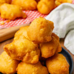 Fried corn fritters stacked on a dark blue plate, with a white napkins.