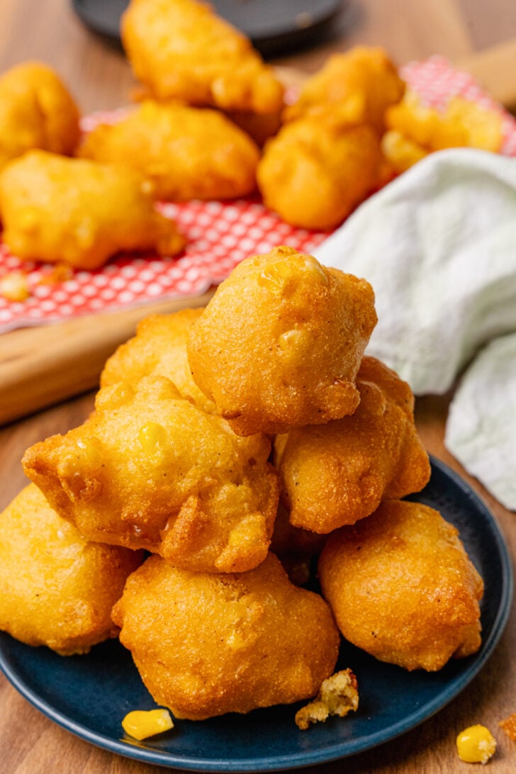 Fried corn fritters stacked on a dark blue plate, with a white napkins.