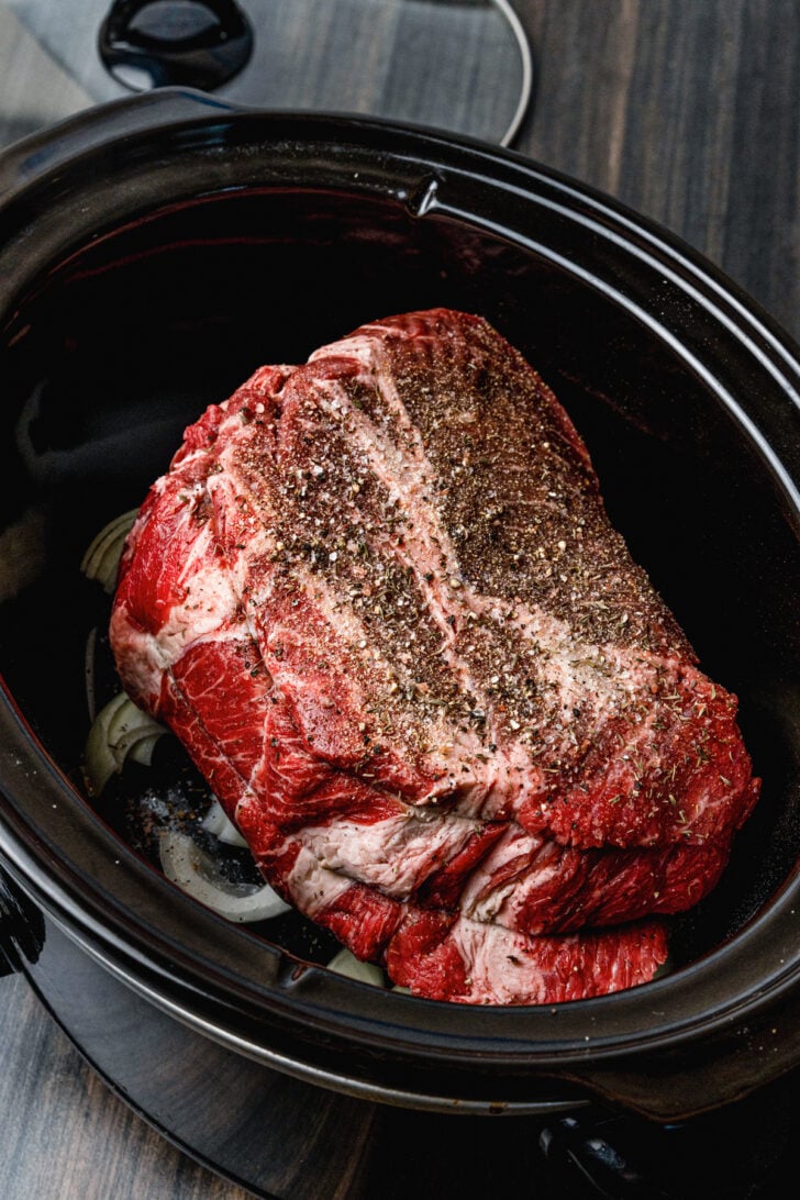 Whole beef roast seasoned with salt and pepper and other seasoning on a layer of onions.