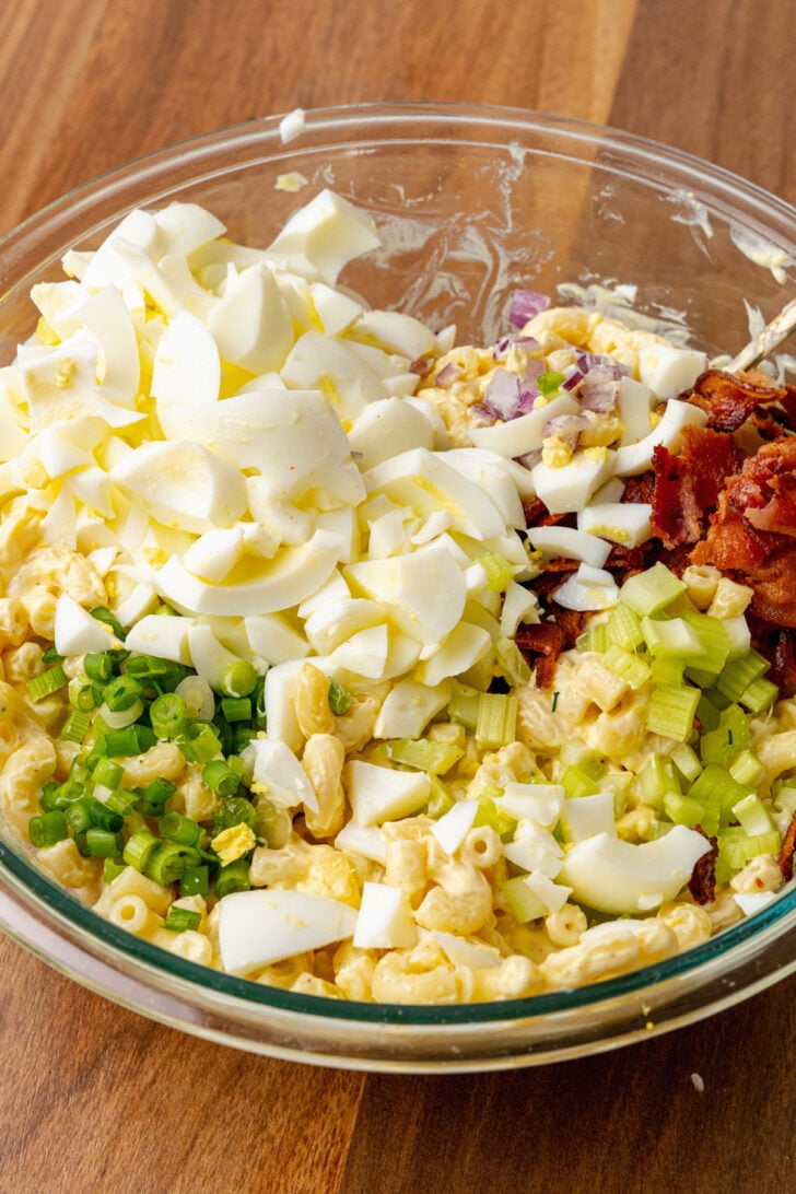 Hard boiled eggs, celery, red onion, bacon, green onions and elbow macaroni in a mixing bowl with a creamy mayonnaise based dressing to make Deviled Egg Pasta Salad.