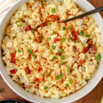 Creamy Deviled Egg Pasta Salad in white bowl with elbow pasta, diced red pimentos, green onions, paprika garnish, and serving spoon on woode