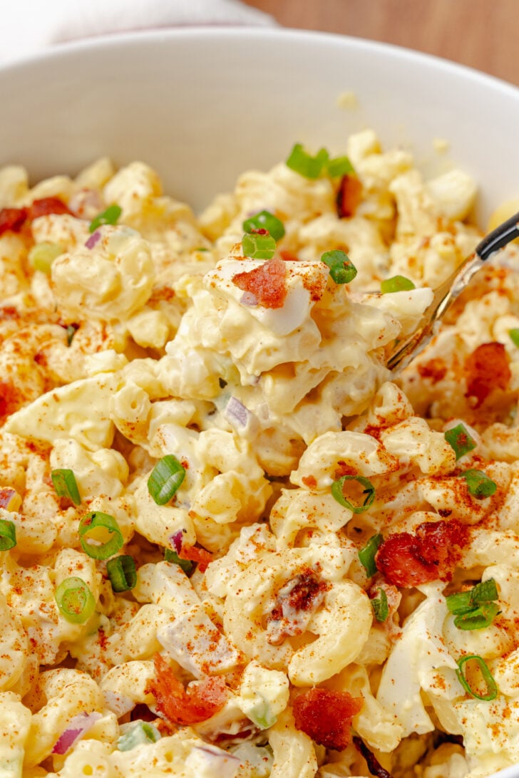 Creamy and full of flavor, Deviled Egg Pasta Salad is a side dish classic that perfect for any family gathering, cookout, or potluck. Made with elbow macaroni, boiled eggs, celery, bacon and topped with green onions all in a delicious mayonnaise based dressing served in a white bowl.