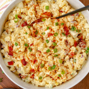 Creamy and full of flavor, Deviled Egg Pasta Salad is a side dish classic that perfect for any family gathering, cookout, or potluck. Made with elbow macaroni, boiled eggs, celery, bacon and topped with green onions all in a delicious mayonnaise based dressing topped with a sprinkle of paprika served in a white bowl.