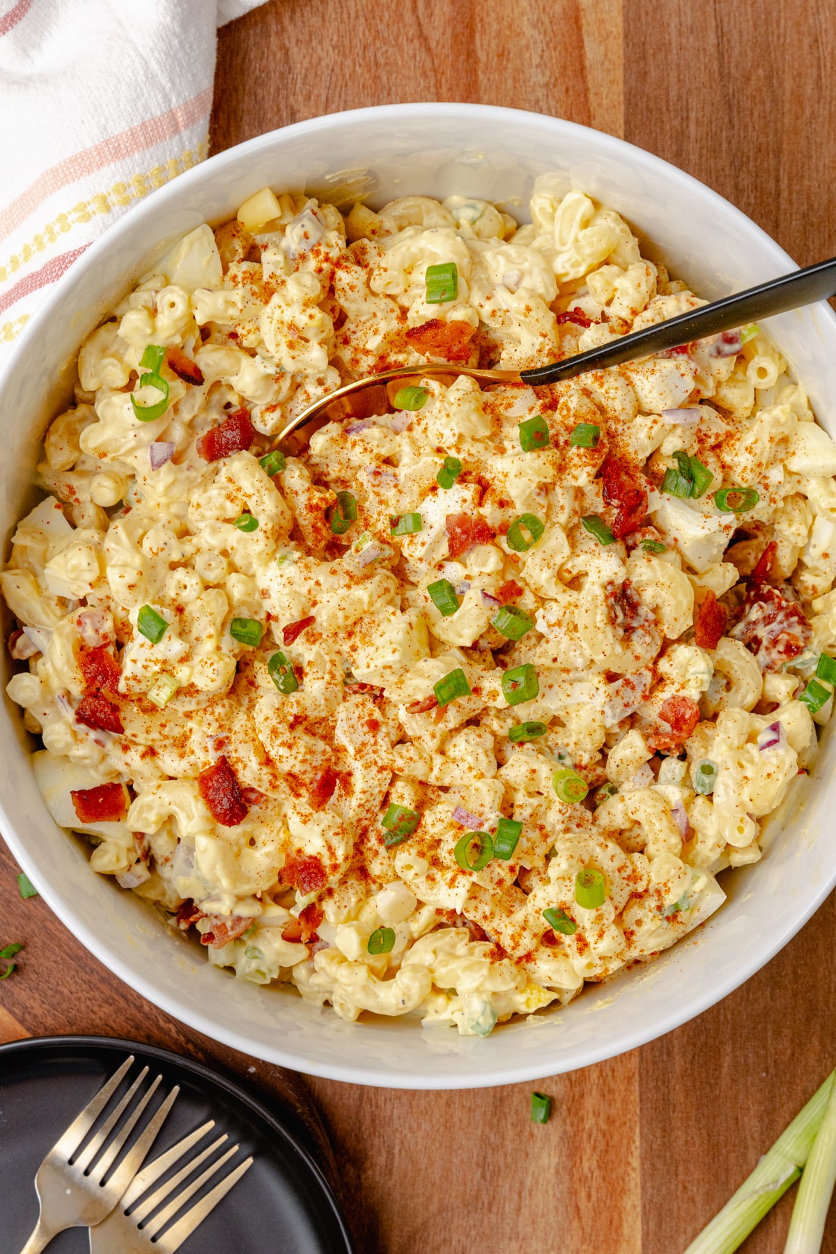 Creamy and full of flavor, Deviled Egg Pasta Salad is a side dish classic that perfect for any family gathering, cookout, or potluck. Made with elbow macaroni, boiled eggs, celery, bacon and topped with green onions all in a delicious mayonnaise based dressing topped with a sprinkle of paprika served in a white bowl.