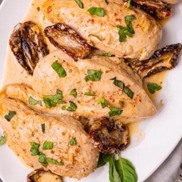 Marry Me Chicken made with chicken breasts, sun dried tomatoes, cooked in a light cream sauce with fresh basil served on a white plate.