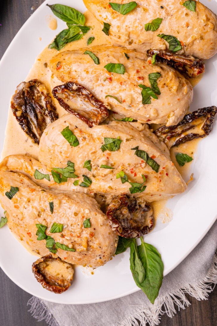 Marry Me Chicken made with chicken breasts, sun dried tomatoes, cooked in a light cream sauce with fresh basil served on a white plate.