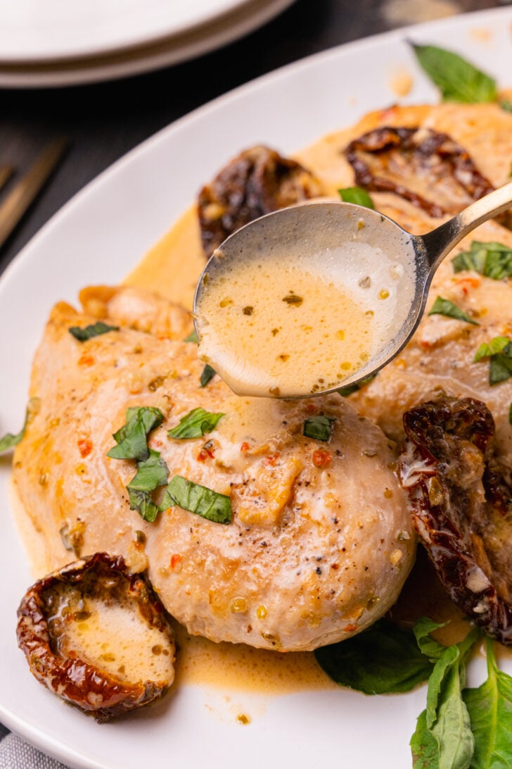Marry Me Chicken made with chicken breasts, sun dried tomatoes, cooked in a light cream sauce with fresh basil served on a white plate.