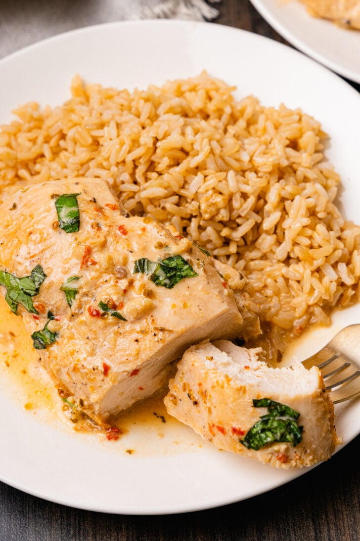 Marry Me Chicken with sun dried tomatoes, fresh basil cooked in a cream sauce served with brown rice for dinner on a white plate is over the top delicious, juicy and tender.