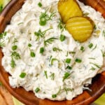 Homemade dill pickle dip served in a wooden bowl with fresh dill and chives garnish along with celery sticks and potato chips.