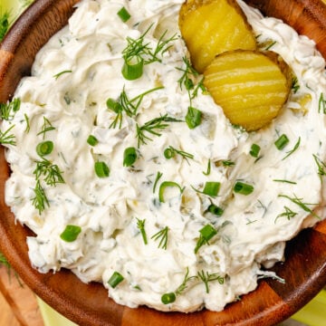 Homemade dill pickle dip served in a wooden bowl with fresh dill and chives garnish along with celery sticks and potato chips.
