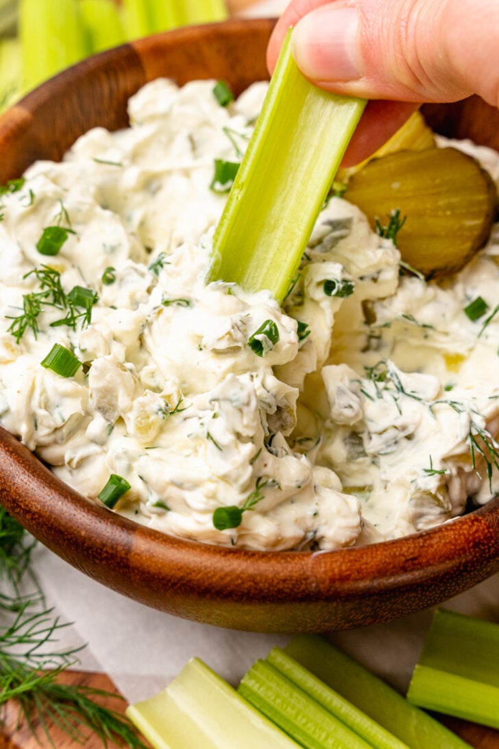 Dill pickle dip with chives and fresh dill being dipped with a celery stick.