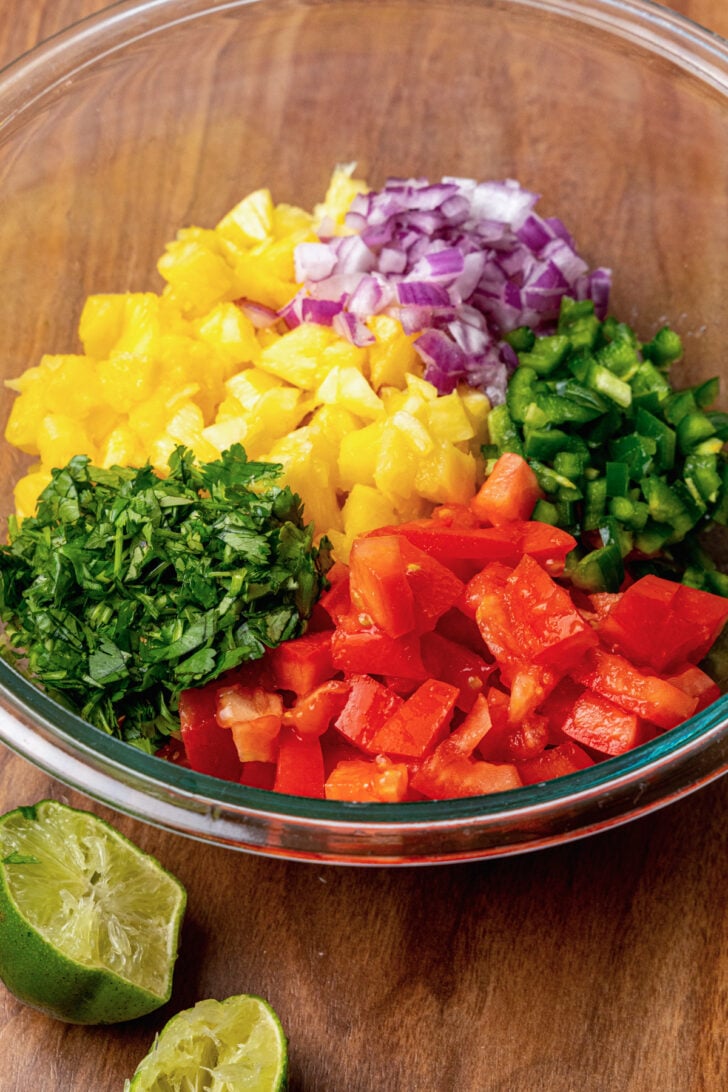 Fresh pineapple, red onion, jalapeno, tomatoes, fresh parsley and lime juice in a bowl to make pineapple salsa.