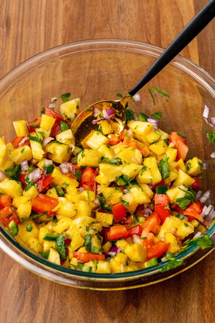 Fresh pineapple and other ingredients in a clear glass bowl stirred together to make pineapple salsa.