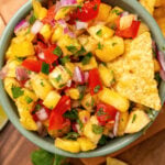 Small bowl of fresh pineapple salsa served with lime wedges and corn tortilla chips.