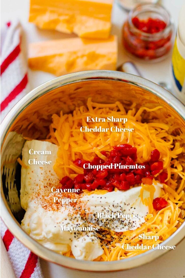 Sharp cheddar cheese, cream cheese, chopped pimentos, extra sharp cheddar cheese, mayonnaise, black pepper and cayenne pepper in a metal bowl for pimento cheese.
