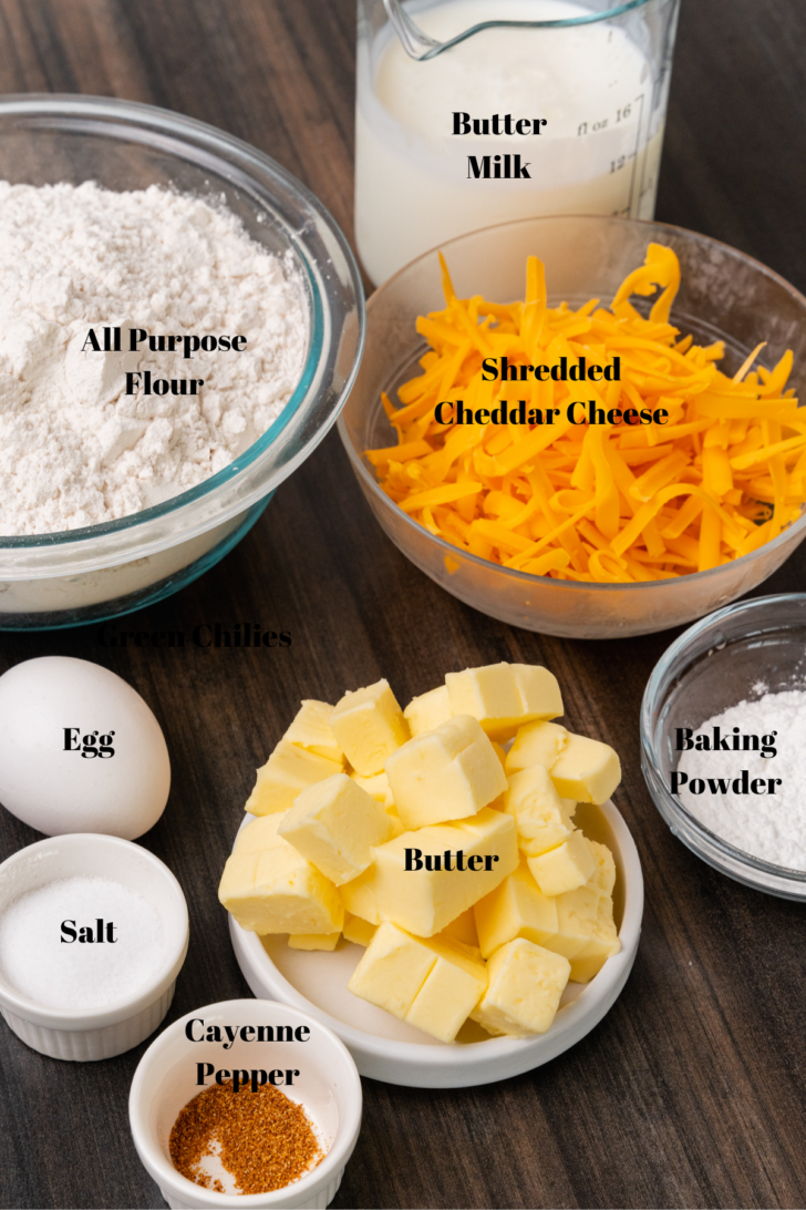 Buttermilk, flour, cheddar cheese, baking powder, butter, cayenne pepper, salt, egg in bowls on a wooden board for cheddar cheese biscuits.