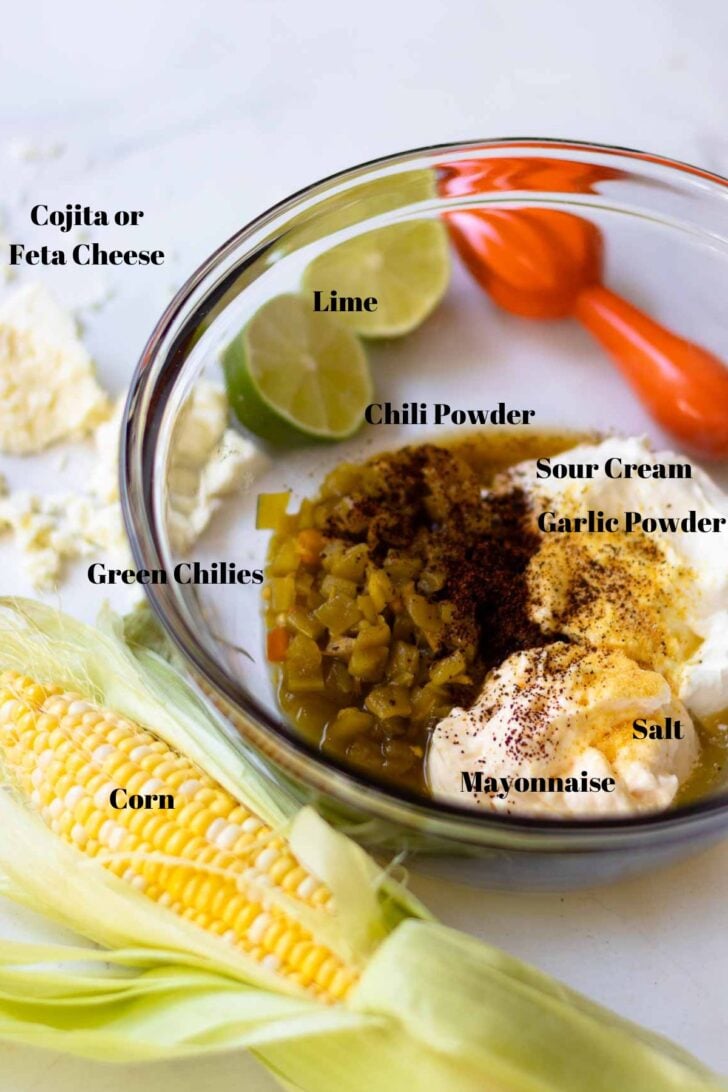 Mexican corn dip ingredients in a glass bowl with corn, lime juice, and cojita cheese.