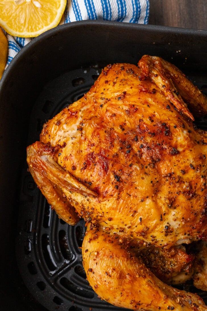 Whole cooked chicken in the basket of an air fryer with golden brown crispy skin.