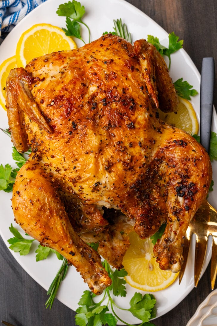 Whole chicken cooked in the air fryer with golden brown crispy skin served on a white platter with lemon slices and fresh parsley.