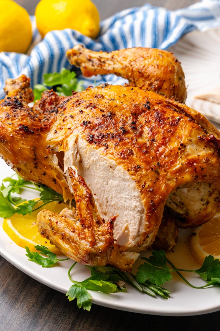 Whole cooked chicken cooked in the air fryer with golden crispy skin, sliced and served on a bed of fresh parsley on a white plate.