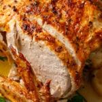 Whole cooked chicken cooked in the air fryer with golden crispy skin, sliced and served on a bed of fresh parsley on a white plate.