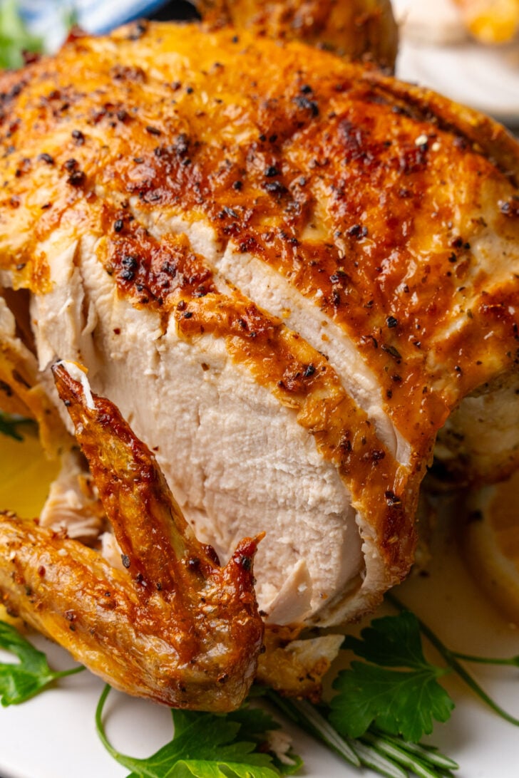 Whole cooked chicken cooked in the air fryer with golden crispy skin, sliced and served on a bed of fresh parsley on a white plate.