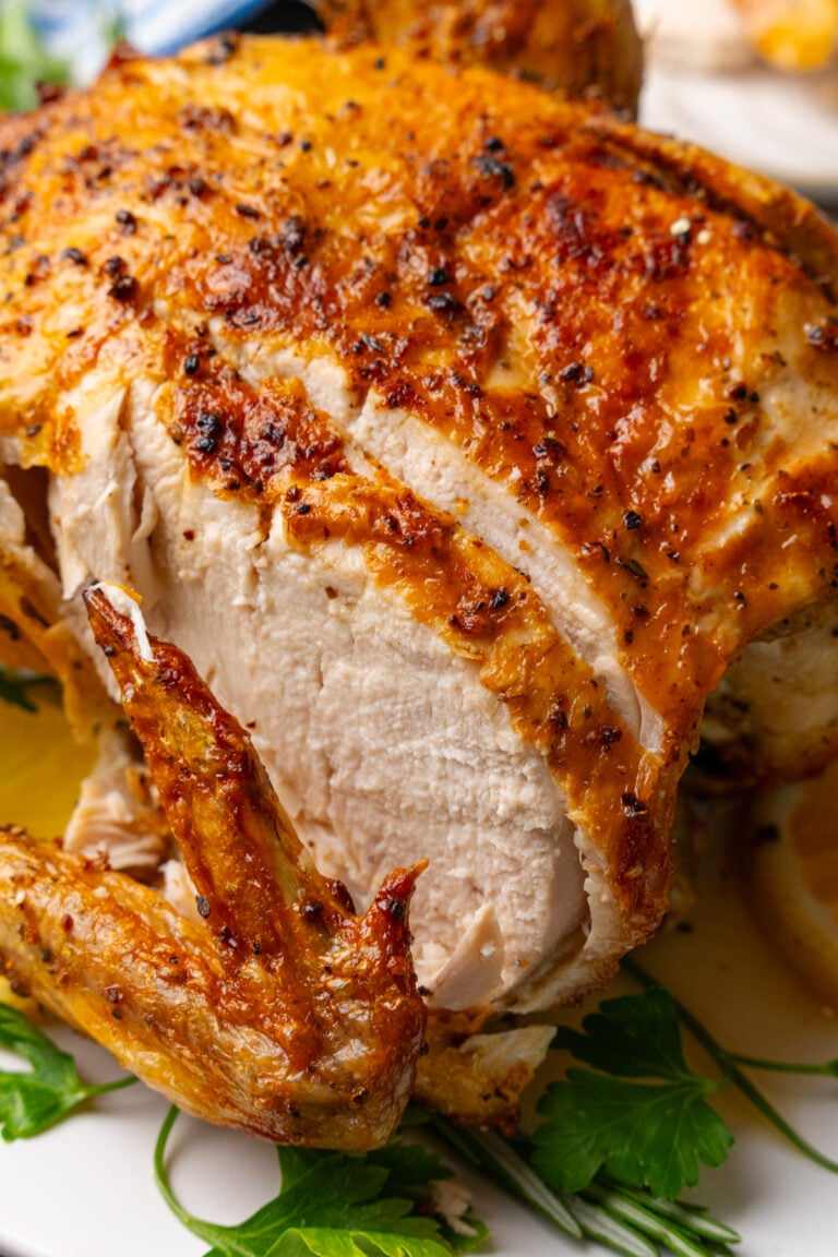 Whole cooked chicken cooked in the air fryer with golden crispy skin, sliced and served on a bed of fresh parsley on a white plate.
