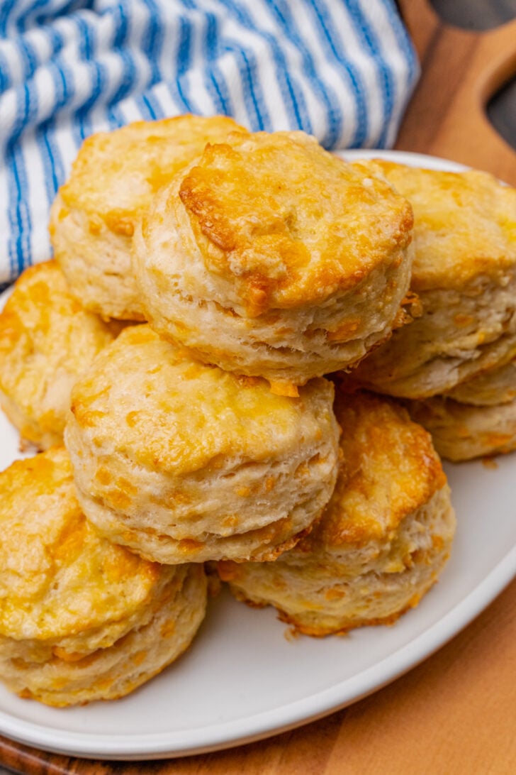 Cheddar cheese biscuits on a white plate that are baked golden brown and brushed with melted butter.