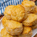 Cheddar cheese biscuits on a white plate that are baked golden brown and brushed with melted butter.
