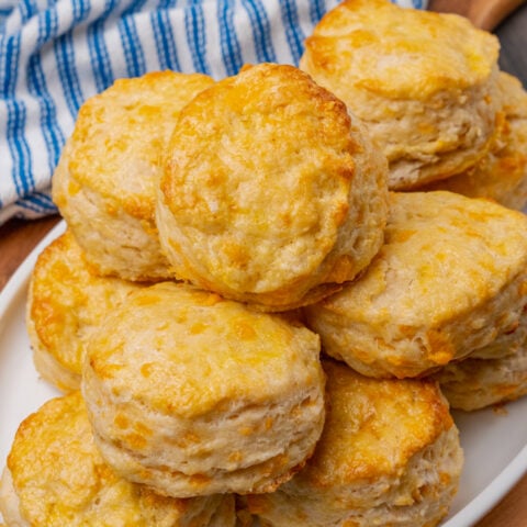 Cheddar cheese biscuits on a white plate that are baked golden brown and brushed with melted butter.