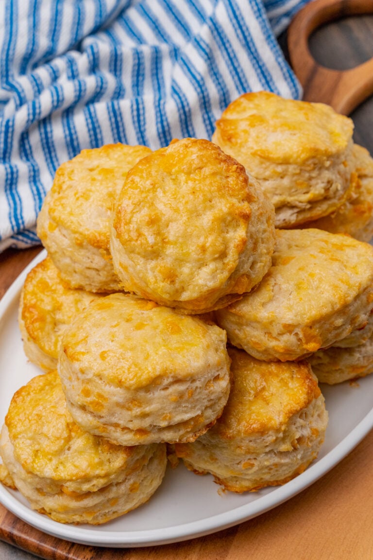 Cheddar cheese biscuits on a white plate that are baked golden brown and brushed with melted butter.