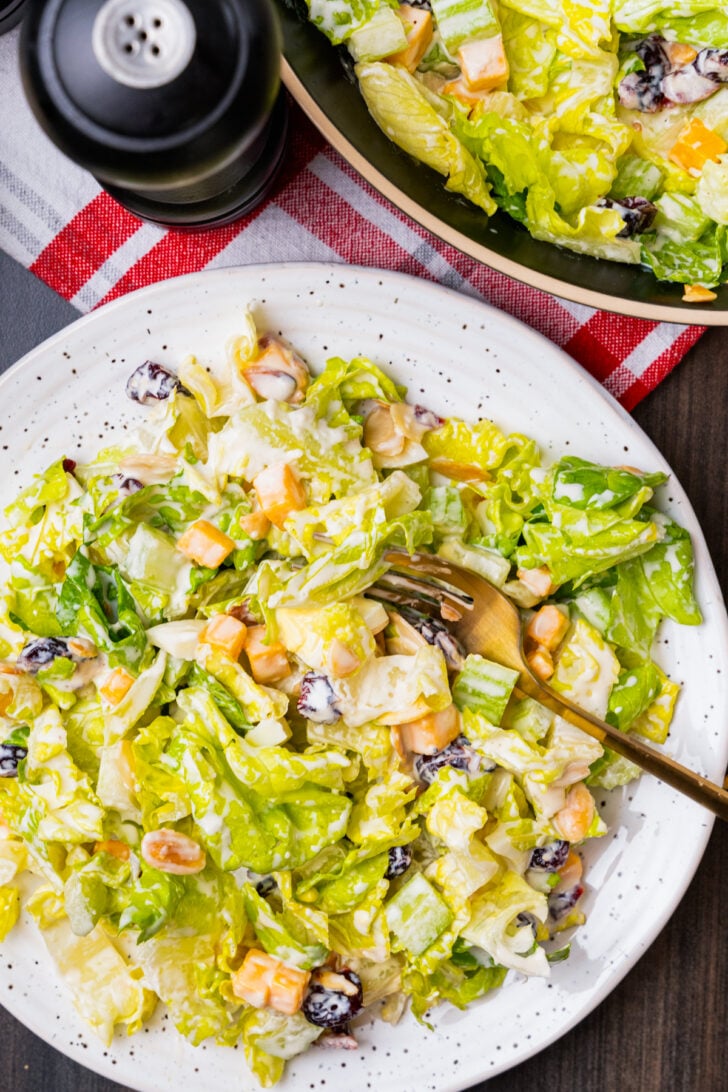 Chopped salad with romaine lettuce, eggs, cubed cheese, cranberries and sliced almonds on a white plate with a gold fork.