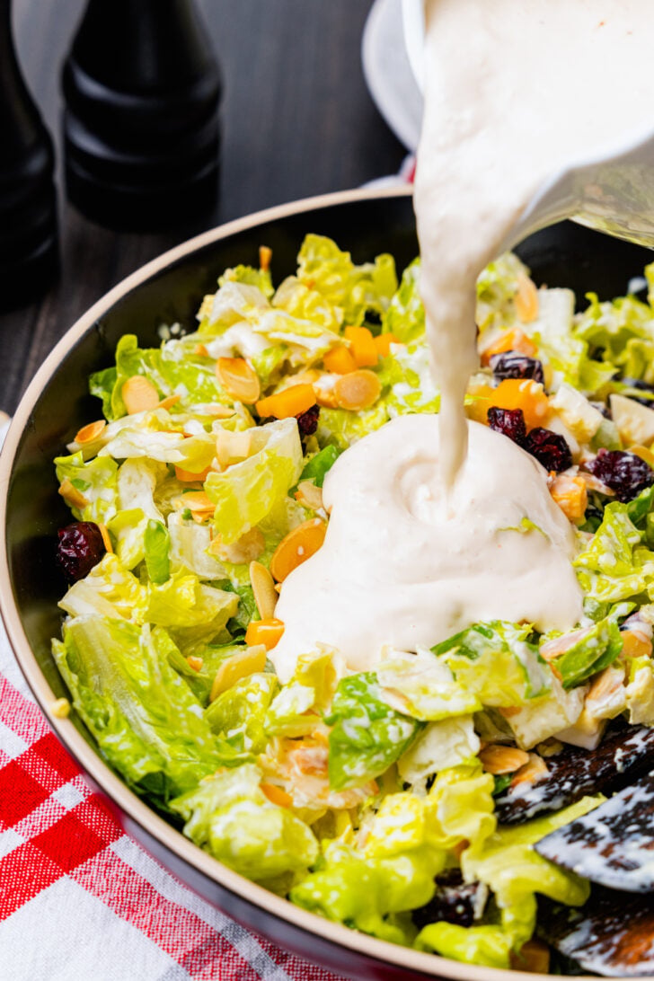 Creamy white dressing poured over chopped romaine, cubed cheese, dried cranberries and sliced almonds in a large black salad bowl.