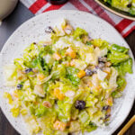 Chopped salad with romaine lettuce, eggs, cubed cheese, cranberries and sliced almonds on a white plate with a gold fork.