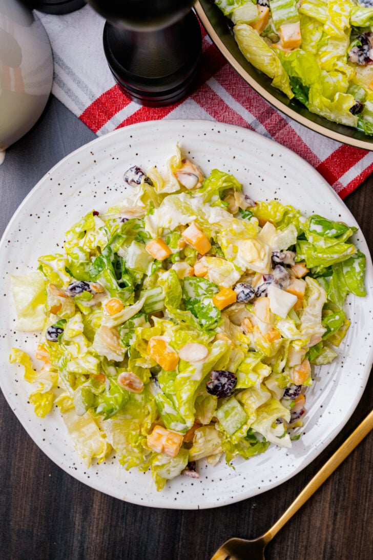 Chopped salad with romaine lettuce, eggs, cubed cheese, cranberries and sliced almonds on a white plate with a gold fork.