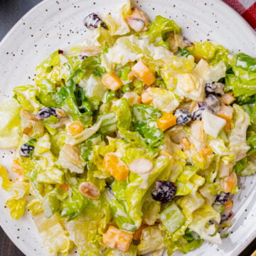 Chopped salad with romaine lettuce, eggs, cubed cheese, cranberries and sliced almonds on a white plate with a gold fork.