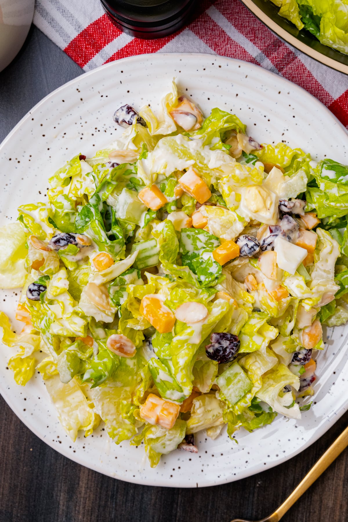 Chopped salad with romaine lettuce, eggs, cubed cheese, cranberries and sliced almonds on a white plate with a gold fork.