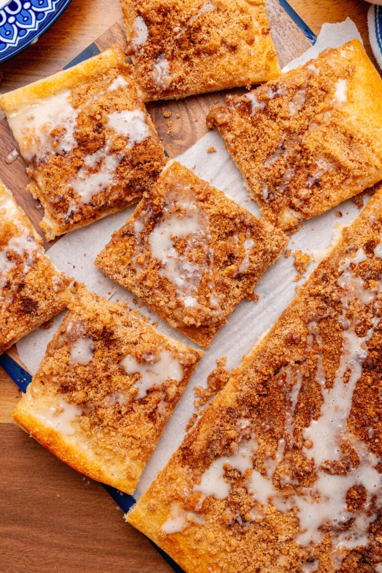 Squares of cinnamon brown sugar pizza topped with vanilla icing on a parchment paper on a wooden board.