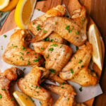 Lemon garlic oven baked chicken wings on a wooden board with lemon slices and topped with chopped parsley.