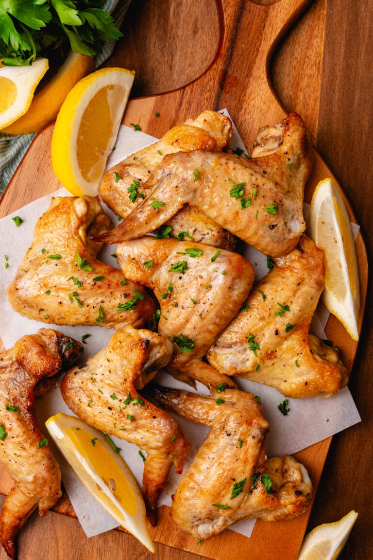 Lemon garlic oven baked chicken wings on a wooden board with lemon slices and topped with chopped parsley.