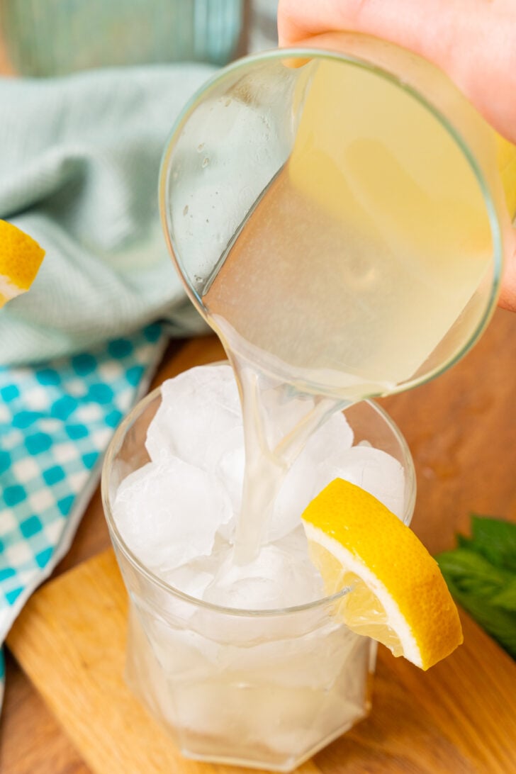 Fresh homemade lemonade being poured over ice in a clear glass with a lemon wedge.