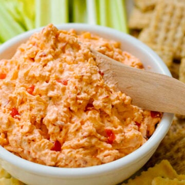 Homemade Pimento Cheese in a white bowl served and wooden knife with saltine crackers and celery sticks on a white platter.